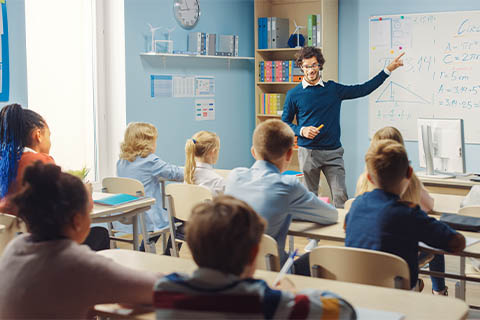 Male teacher pointing at white board teaching class of students